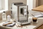 Machine à café en inox sur un comptoir avec produits d'entretien, une tasse de café et un carnet.