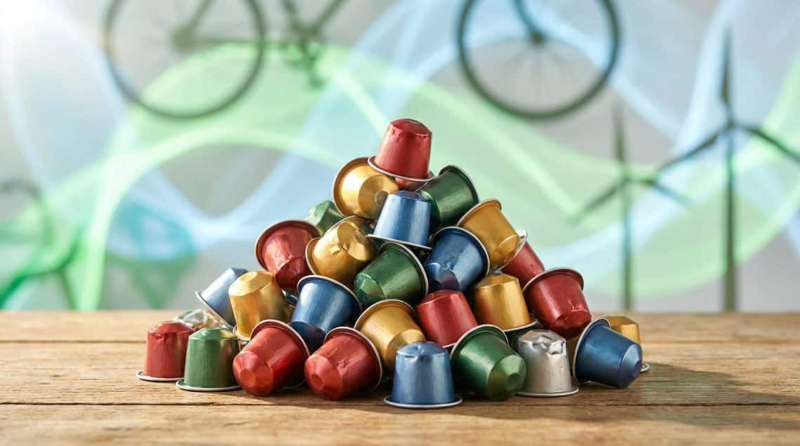 Tas de capsules de café en aluminium colorées empilées sur une table en bois avec un arrière-plan écologique.
