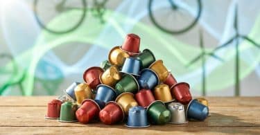 Tas de capsules de café en aluminium colorées empilées sur une table en bois avec un arrière-plan écologique.