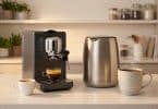 Une machine à café expresso noire à côté d'une bouilloire en acier inoxydable et deux tasses sur un comptoir de cuisine.