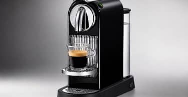 Machine à café Nespresso noire moderne avec une tasse d'espresso en verre sur le socle, sur fond gris.