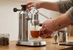 Mains utilisant une machine à expresso manuelle en acier inoxydable pour verser un café dans une tasse orange.