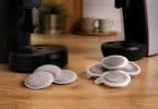 Deux machines à café sur un plan de travail avec des dosettes souples à gauche et des capsules en plastique à droite.