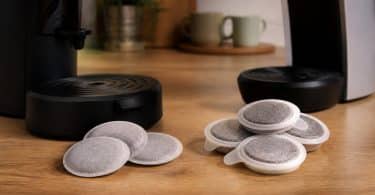 Deux machines à café sur un plan de travail avec des dosettes souples à gauche et des capsules en plastique à droite.
