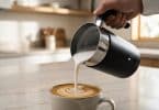 Une main verse une mousse de lait onctueuse d'un mousseur électrique noir dans une tasse de café avec un latte art.