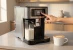Une main sélectionne un expresso sur l'écran tactile d'une machine à café automatique avec carafe à lait intégrée.