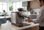 Un employé prépare un café avec une machine à grain en inox dans une cuisine de bureau moderne.