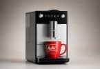 Machine à café à grain Melitta noire et argentée avec une tasse rouge logotée, sur fond gris neutre.