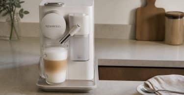 Machine à café Nespresso blanche sur un plan de travail avec un verre de cappuccino fraîchement préparé.