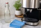 Une cafetière expresso moderne sur un comptoir en marbre avec une bouteille d'eau et une plante.