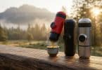 Trois machines expresso portables colorées sur une table en bois avec un café fumant face à un paysage de montagne.