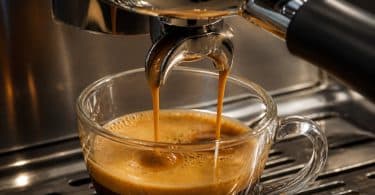 Gros plan sur deux filets de café espresso coulant d'une machine dans une tasse en verre transparente.
