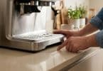 Une personne pointe du doigt une flaque d'eau s'échappant sous une machine à café en acier inoxydable sur un comptoir.