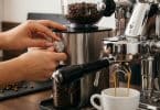 Mains réglant la finesse de mouture sur un broyeur à café inox, à côté d'une machine expresso professionnelle.