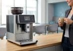 Une employée en costume sourit en tenant une tasse de café fumante près d'une machine à café automatique moderne.