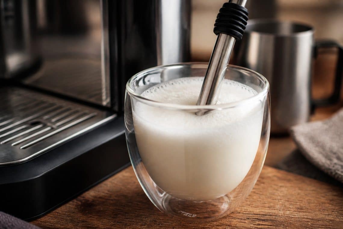 Buse vapeur de machine &agrave; caf&eacute; plongeant dans un verre de lait mousseux &agrave; c&ocirc;t&eacute; d'une machine professionnelle.