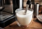 Buse vapeur de machine à café plongeant dans un verre de lait mousseux à côté d'une machine professionnelle.