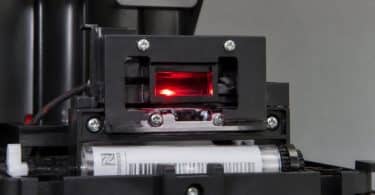 Gros plan sur le lecteur optique rouge d'une machine Nespresso Vertuo lisant le code-barres d'une capsule.