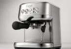Machine à expresso Sage compacte en acier brossé avec porte-filtre noir et buse vapeur sur fond gris clair.