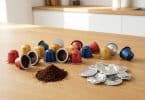 Capsules de café Nespresso colorées sur une table en bois avec du marc de café et des opercules en aluminium recyclés.