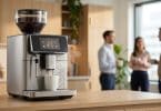 Une machine à café automatique moderne coulant un café sur un comptoir dans une cuisine de bureau avec des collègues.