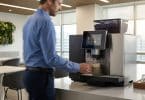 Un employé utilisant une machine à café à grains automatique moderne dans une cuisine d'entreprise lumineuse.