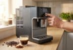 Une main règle une machine à café à grain posée sur un plan de travail en bois avec une tasse de café à côté.