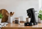 Une cafetière Senseo noire en train de préparer un café sur un comptoir de cuisine en bois.