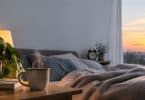 Une tasse de café fumante sur une table de chevet près d'un lit douillet au lever ou au coucher du soleil.