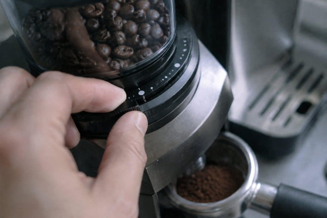 Main ajustant la bague de réglage de mouture sur un moulin à café DeLonghi avec des grains dans le réservoir.