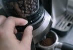 Main ajustant la bague de réglage de mouture sur un moulin à café DeLonghi avec des grains dans le réservoir.
