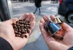 Mains tenant des grains de café d'un côté et des capsules colorées de l'autre, avec une rue floue en arrière-plan.