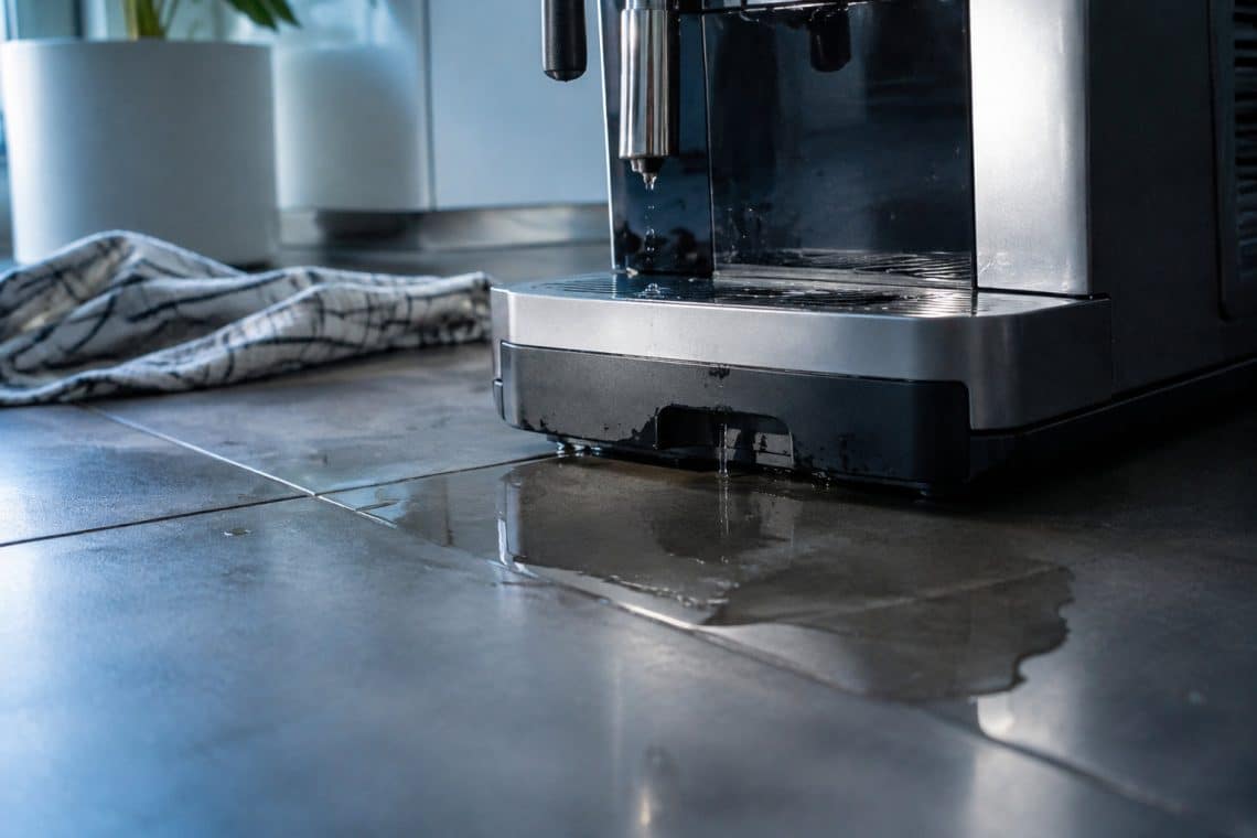 Une machine &agrave; caf&eacute; DeLonghi fuit sur le plan de travail, formant une flaque d'eau avec un torchon &agrave; proximit&eacute;.