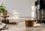 Une tasse de café sur un comptoir à côté d'une machine à café automatique et de grains de café éparpillés.