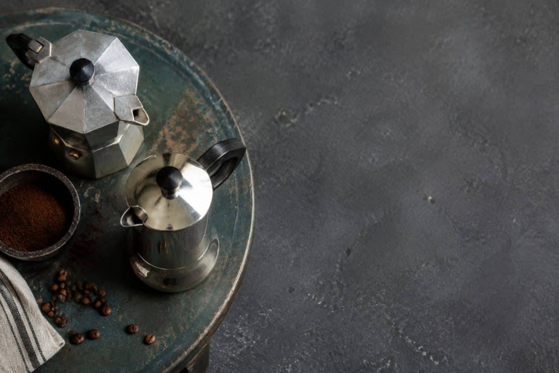 Vue de dessus de deux cafetières italiennes, l'une en aluminium et l'autre en inox, posées sur une table en bois.