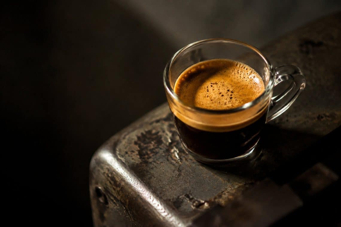 Une tasse d'expresso fra&icirc;chement pr&eacute;par&eacute; avec une cr&egrave;me &eacute;paisse, pos&eacute;e sur une surface m&eacute;tallique sombre et textur&eacute;e.
