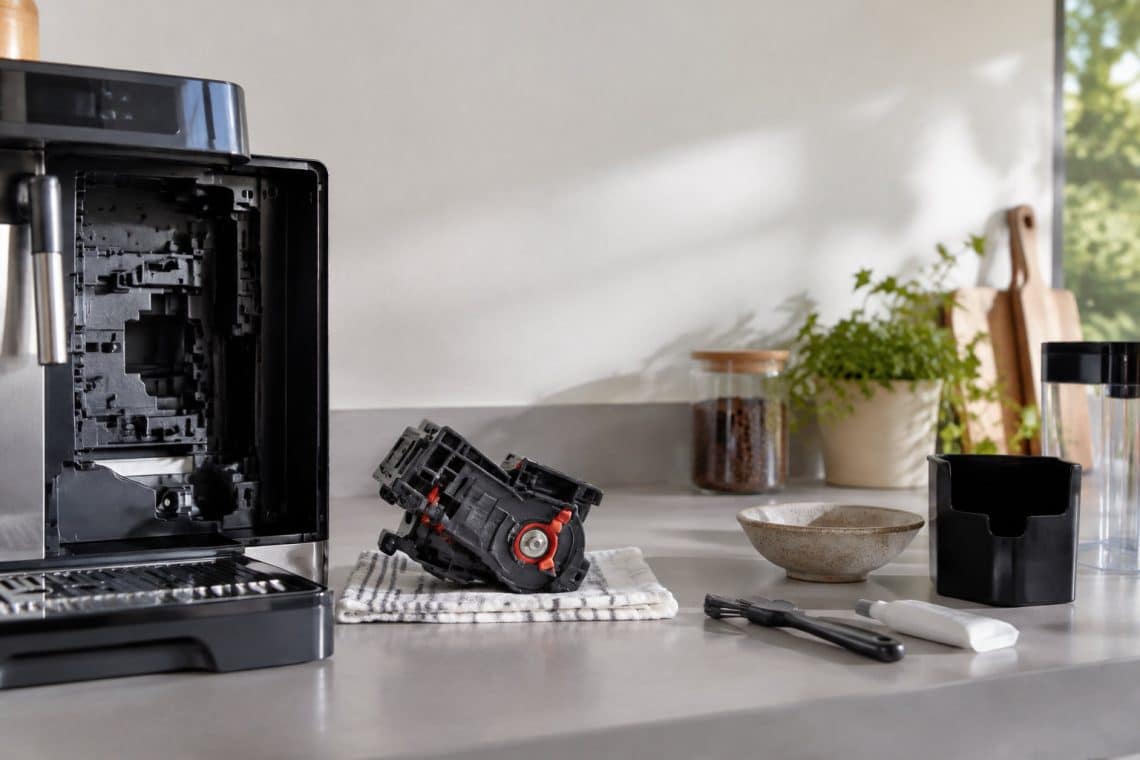 Groupe caf&eacute; amovible d'une machine DeLonghi pos&eacute; sur un torchon &agrave; c&ocirc;t&eacute; d'une brosse de nettoyage et d'un tube de graisse.
