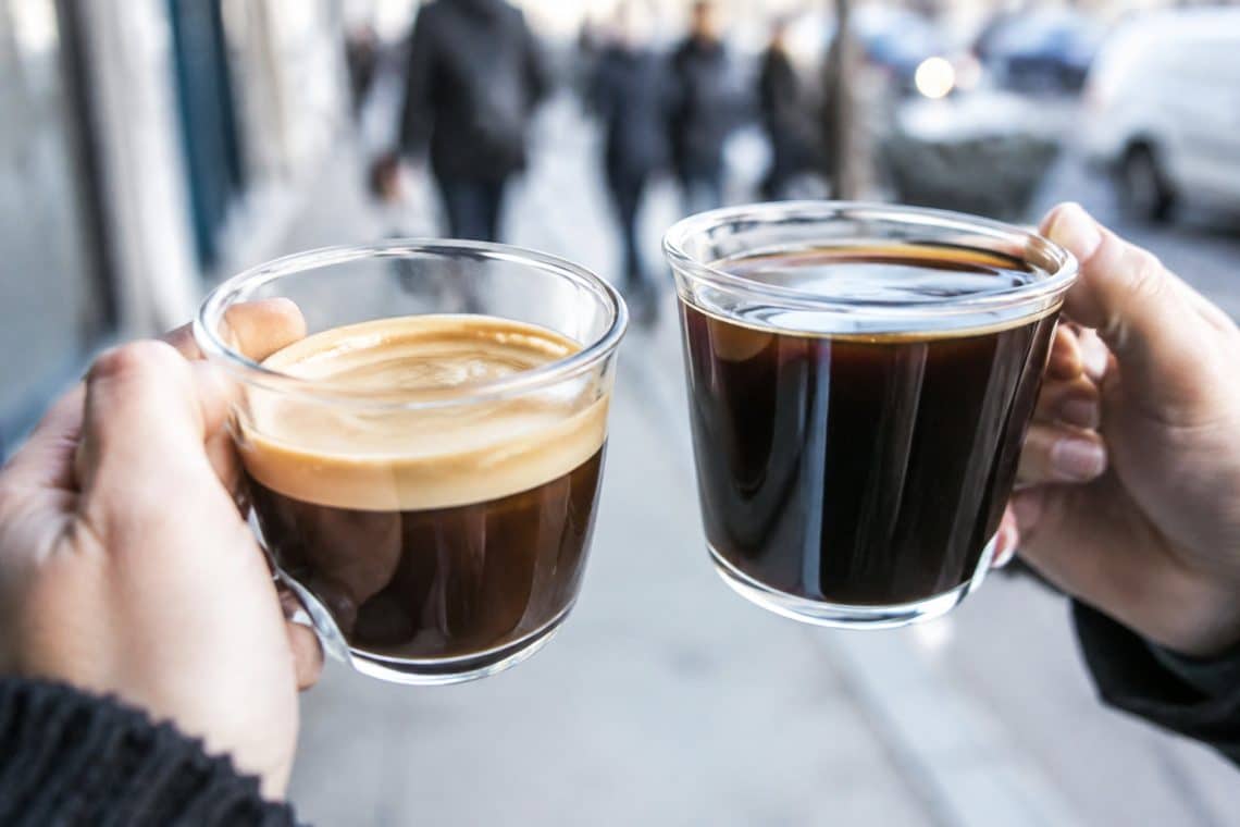 Deux mains tiennent chacune une tasse en verre contenant un caf&eacute;, l'un avec une mousse &eacute;paisse et l'autre noir profond.