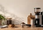 Un porte-filtre rempli de café moulu posé sur une table en bois, à côté d'un moulin et d'un bol de grains de café.