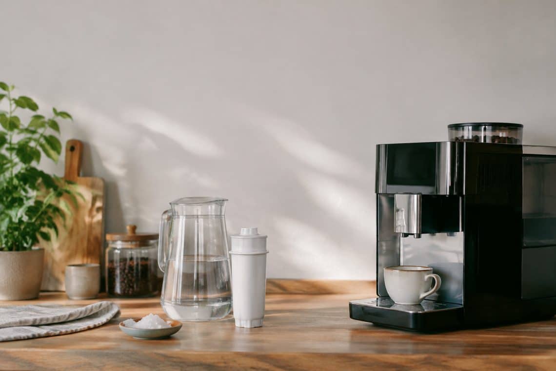 Une machine &agrave; caf&eacute; moderne avec une cartouche filtrante, une carafe d'eau et une tasse sur un plan de travail en bois.
