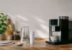 Une machine à café moderne avec une cartouche filtrante, une carafe d'eau et une tasse sur un plan de travail en bois.