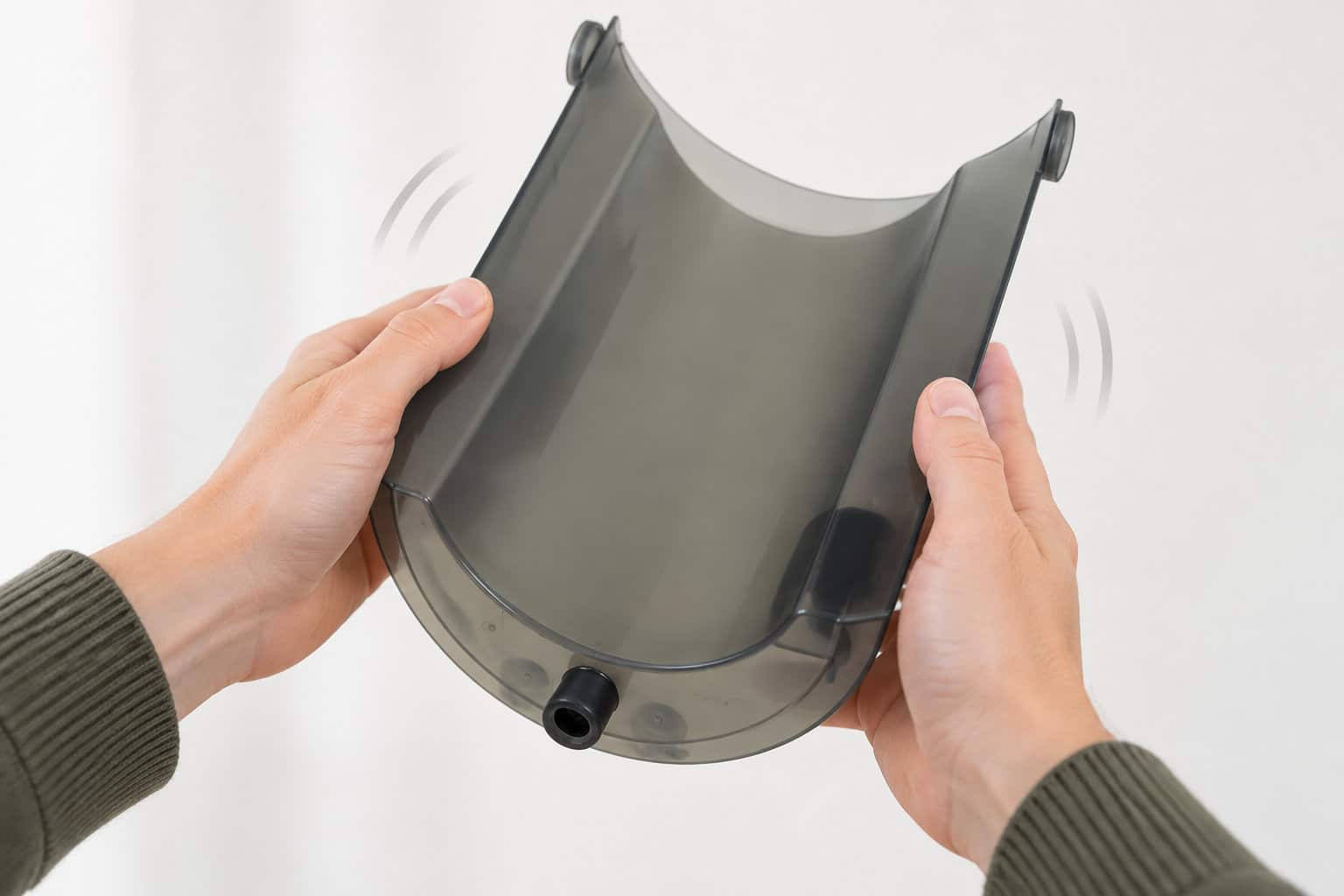 Deux mains tiennent un r&eacute;servoir en plastique gris fum&eacute;, avec une ouverture munie d&rsquo;un bouchon noir au bas de la pi&egrave;ce.