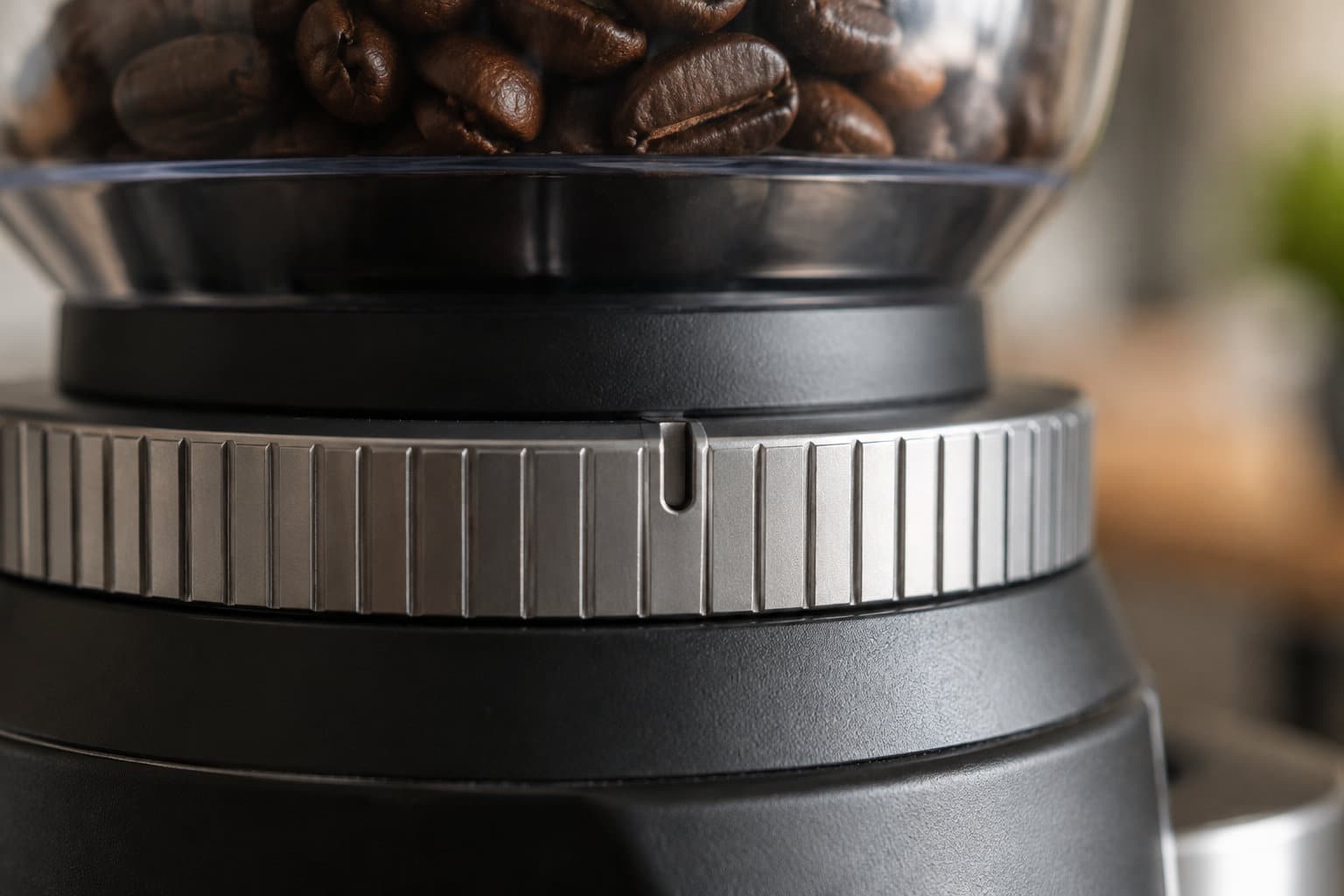 Gros plan sur un moulin à café rempli de grains de café, avec sa bague de réglage métallique.