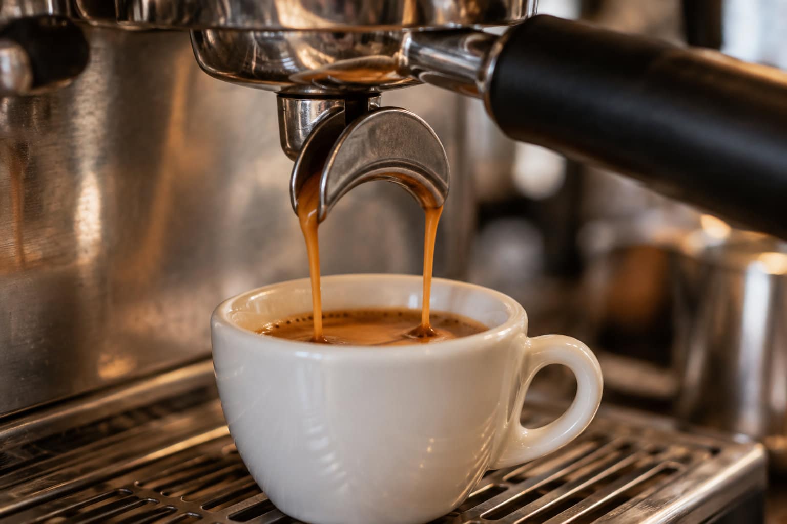 Deux filets de caf&eacute; s&rsquo;&eacute;coulent d&rsquo;une machine &agrave; espresso dans une tasse blanche pos&eacute;e sur la grille.