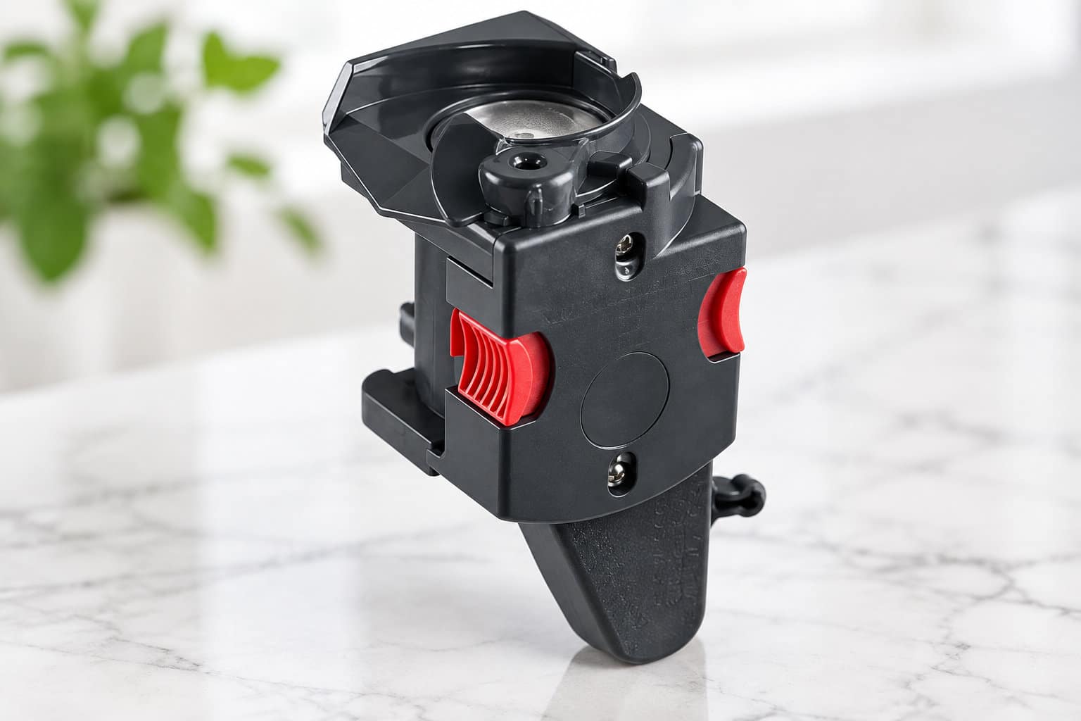 Un dispositif m&eacute;canique noir avec des boutons rouges est pos&eacute; sur une surface blanche vein&eacute;e, devant une plante floue.